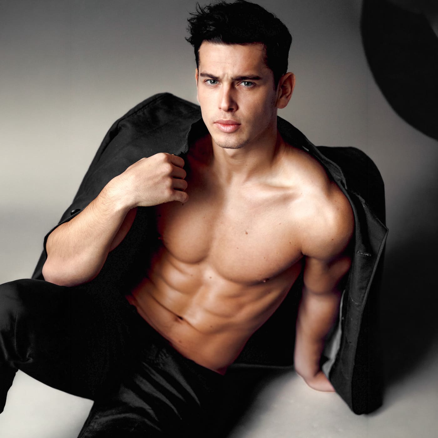 Shirtless man with a defined chest holding a black jacket over his shoulder