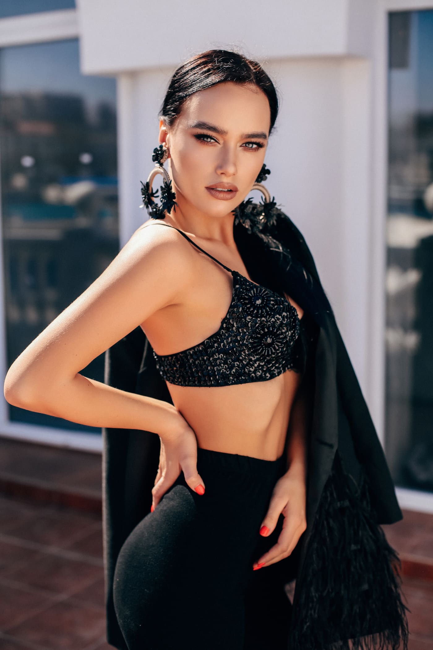 Woman in a beaded black crop top and high-waisted trousers with a jacket over one arm