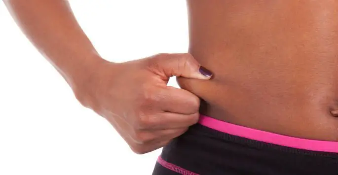 A close-up image of a person pinching a small amount of belly fat on their abdomen.