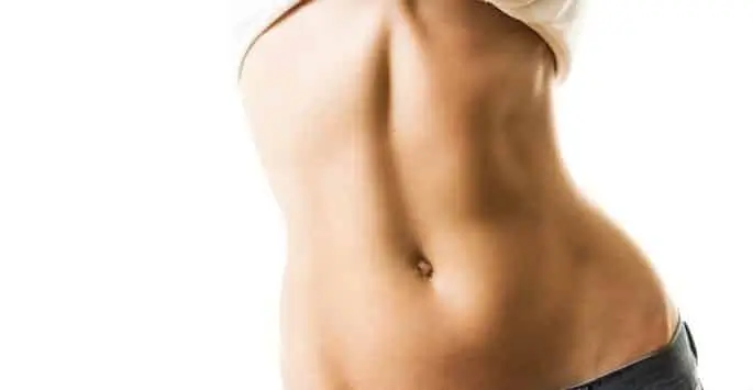 Side view of a woman's bare torso showing her ribs and toned abdomen, wearing low-rise jeans and lifting her white shirt.
