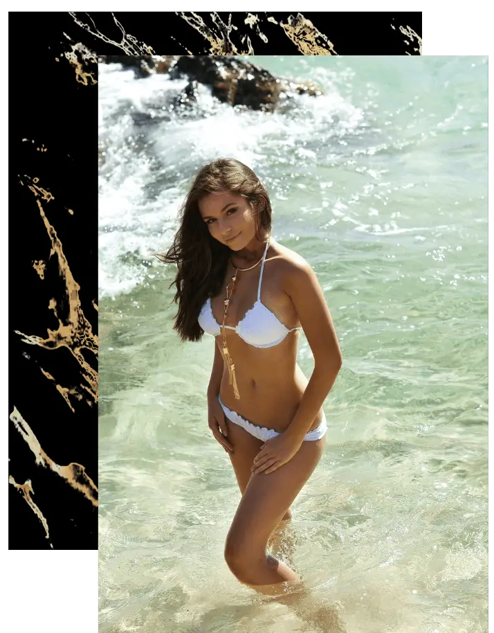 A woman with white bikini and a gold neckless standing on the beach.